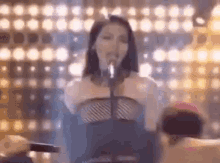a woman is singing into a microphone on a stage in front of a crowd of people .