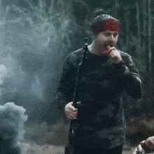a man with a bandana on his head is holding a rifle and eating something
