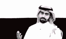 a man with a beard wearing a head scarf and a white shirt stands in front of a wall with pink hearts on it