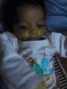 a baby in a white shirt with a blue flower on it