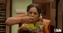 a woman is eating food from a plate with the xhk logo in the corner
