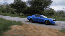 a blue car is driving down a dirt road with trees in the background