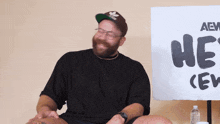 a man sitting in front of a sign that says " he 's "