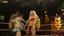 two women in bikinis are wrestling in a wrestling ring with a nxt logo in the background