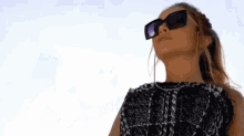a woman wearing sunglasses and a plaid shirt looks up at the sky