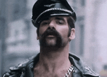 a man with a beard and mustache is wearing a hat and leather jacket .