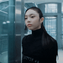 a woman wearing a black turtleneck and earrings has the letter a on her belt