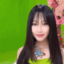 a woman with long black hair and a flower necklace is smiling in front of a green background .