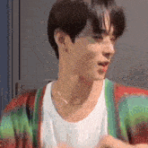 a young man wearing a green and red cardigan and a white shirt is looking at the camera .