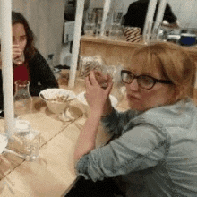 a woman wearing glasses is sitting at a table holding a glass of water .