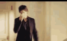 a man in a suit is standing in a hallway holding his nose .