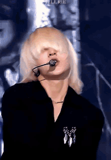 a woman with blonde hair is wearing a black shirt and a microphone in her mouth
