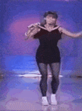 a woman in a black dress is dancing and singing into a microphone