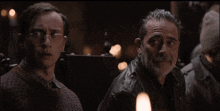 a man with glasses sits next to a man with a beard in a dark room