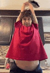 a man in a red shirt is standing in a kitchen with his arms up .