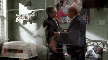 two men are standing in a room with a picture of a family on the wall behind them with #theblacklist on it