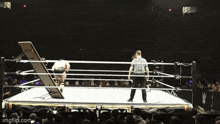 a referee stands in the middle of a wrestling ring with a table in the middle