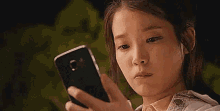 a woman is holding a cell phone in her hand and looking at it .