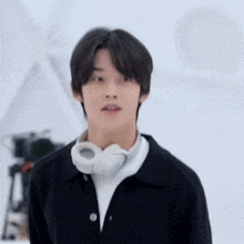 a young man wearing headphones around his neck is standing in front of a white wall .