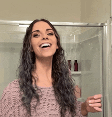 a woman in a pink sweater is smiling in front of a shower stall
