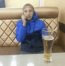 a man in a blue jacket is talking on a cell phone next to a full glass of beer