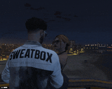 a man wearing a sweatbox los santos sweatshirt looks at a woman