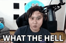 a man wearing headphones is sitting in front of a microphone with the words `` what the hell '' written on the screen .