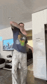 a man in a blue shirt and white pants is dancing in a living room in front of a television .