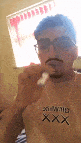 a man wearing glasses and a t-shirt that says xxx is brushing his teeth