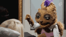 a stuffed animal with a purple feather on its head holds a pendulum