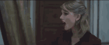taylor swift is wearing red lipstick and looking at herself in a mirror .