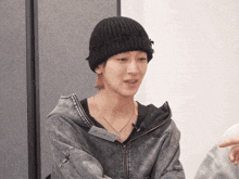 a man wearing a black beanie and a grey jacket has a name tag on his neck that says ' hongye '