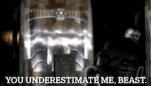 a man in a suit is standing in front of a machine and says you underestimate me beast .