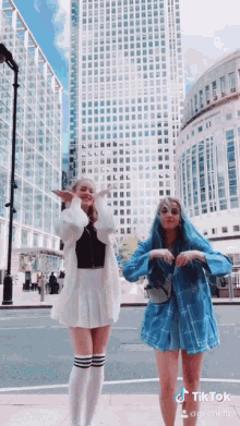 two girls are dancing in front of a tall building on a street .