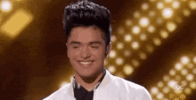 a young man in a tuxedo and bow tie is smiling on stage .