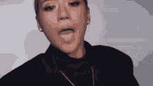 a woman wearing a black turtleneck sweater and a necklace is making a funny face .