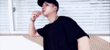 a man wearing a black hat and a black t-shirt is licking his lips