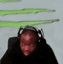 a man wearing headphones looks at the camera with a green background behind him