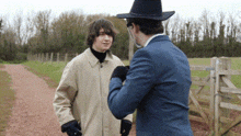 a man in a cowboy hat talks to another man on a dirt road