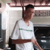 a young man in a white shirt is standing in front of a black car