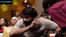 a man with a beard is sitting in front of a crowd and a woman is standing next to him .