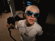 a man wearing sunglasses and a white shirt is pumping gas into his car .