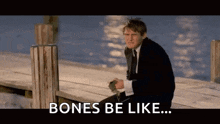 a man in a suit and tie is sitting on a dock with the words `` bones be like '' written on the screen .