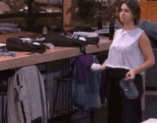 a woman in a striped shirt is standing in front of a table holding a bottle .