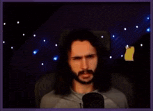 a man with long hair and a beard is sitting in front of a microphone making a funny face .