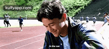 a man is sitting on a track and smiling while a group of people run in the background .