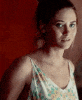 a woman in a floral dress is standing in front of a red wall and looking at the camera .