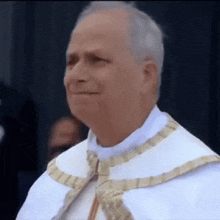 a man in a white robe and gold trim is smiling