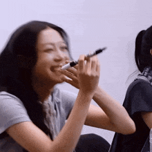 a woman holds a marker in her mouth while another woman looks on