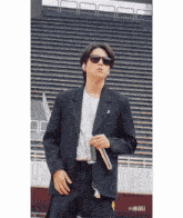 a man wearing sunglasses and a suit is holding a microphone in front of a stadium .